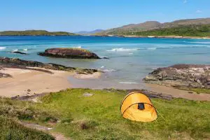 An orange tent pitched overlooking a beach and sapphire blue sea in Co Kerry Ireland
